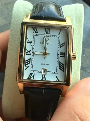 GANT rektangulär klocka i guld och svart - Stilren klocka från GANT med rektangulärt guldfärgat boett, vit urtavla med svarta romerska siffror och datumvisning. Svart läderarmband med klassisk struktur. Perfekt accessoar för dig som gillar tidlös design.