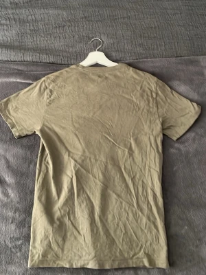 Olivegrön t-shirt från Levi's - Säljer en enkel beige t-shirt från Levi's med klassisk rund hals och liten röd Levi's-logga på bröstet. T-shirten är i mjuk bomull och har en normal passform med korta ärmar. Perfekt till jeans eller shorts.