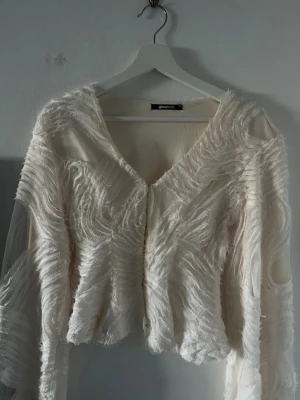 Vit meshblus med struktur från Gina Tricot - Unik vit meshblus från Gina Tricot med långärmad design och coola strukturerade detaljer över hela tyget. Blusen har v-ringning och transparenta partier som ger en trendig och edgy look. Perfekt för dig som vill sticka ut med din stil.