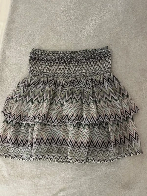 Missoni volangkjol från KappAhl - Säljer en fin kort kjol från KappAhl med missoni mönster. zigzag-mönster i svart, vitt, lila och grönt. Kjolen har bred smock i midjan och dubbla volanger. Står storlek 146-152 men passar även som xs. Kjolen går även att använda som tubetop.