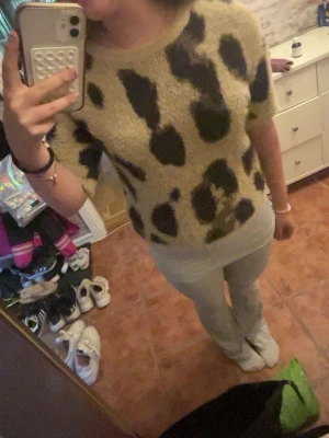 Leopardmönstrad stickad tröja - Säljer en fluffig stickad tröja med leopardmönster i beige och svart. Tröjan har korta ärmar, rund halsringning och är gjord i ett mjukt, lurvigt material som känns riktigt cozy. Perfekt för dig som vill sticka ut med ett djurmönster i garderoben.