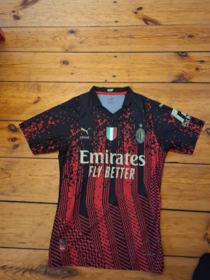 AC Milan matchtröja svart/röd Puma - Snygg AC Milan matchtröja från Puma i svart och rött med digitalt mönster. Tröjan har korta ärmar, klubbmärke, sponsortryck och italienska flaggan på bröstet. Tillverkad i lätt och funktionellt material som passar perfekt till fotbollsträning.sitter tight på mig som är 190cm och 80kg