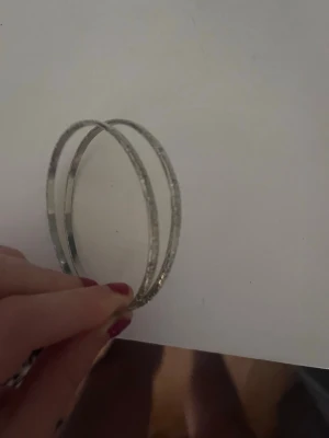 Tunna silvriga bangles armband - Två stilrena, tunna armband i silverfärg med lätt texturerad yta. De är runda och passar perfekt för att stapla flera tillsammans eller bära ensamma för en minimalistisk look. Materialet ser ut som metall och designen är enkel men ändå elegant.