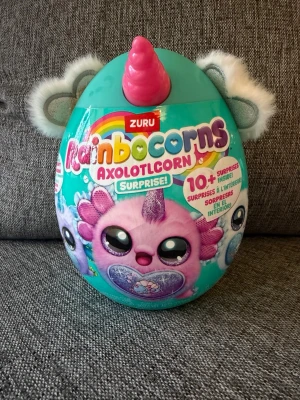 NY! Rainbocorns Axolotlcorn Surprise - Ny oöppnad!  Rainbocorns Axolotlcorn Surprise är en leksak som innehåller över 10 överraskningar. Denna produkt är en del av Rainboville-serien och innehåller en mjuk axolotl-plysch, klistermärken och slime.