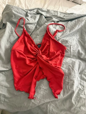 Röd croppad linnetopp med knyt - Snygg röd linnetopp med smala axelband och v-ringning. Toppen har ett twistat knyt framtill och asymmetrisk, croppad nederkant. Perfekt för sommaren och ger en trendig vibe till din outfit.