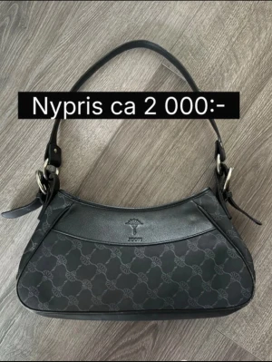 JOOP! väska - JOOP! Elegant baguetteväska i svart  Nypris: ca 2 000 kr  Snygg och stilren JOOP!-väska i klassisk svart färg. Väskan är tillverkad i slitstarkt tyg med märkets monogrammönster och har detaljer i silverfärgad metall. Den har en kort, bekväm axelrem och en elegant baguetteform som gör den enkel att bära både till vardags och finare tillfällen.  Väskan är rymlig för sin storlek och har plats för det viktigaste. Skicket är mycket gott med normala tecken på användning.  Färg: Svart Märke: JOOP! Stil