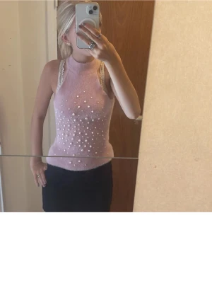 Ljusrosa pärlprydd topp från Zara - Supersöt ljusrosa ärmlös topp från Zara med hög hals och pärldetaljer framtill. Toppen är fluffig och mjuk, vilket ger en mysig känsla. Perfekt för dig som vill sticka ut med en unik och trendig look.
