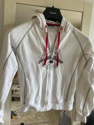 Barn kofta hoodie med dragkedja och tryck - Snygg vit barn  kofta hoodie med dragkedja och gråa sömmar. Framsidan har ett tryck med texten 'Archie Dare' och luvan har röda snören. Två fickor framtill och ribbade muddar vid ärmslut och nederkant. Perfekt för en avslappnad stil.för ålder  från ca 8-9 år