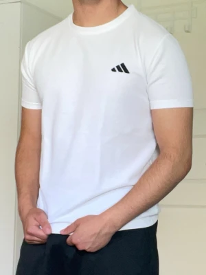 Vit t-shirt från Adidas - Säljer en stilren vit t-shirt med Adidas loggan på bröstet. T-shirten har rund halsringning och korta ärmar. Perfekt för en clean och sportig look.