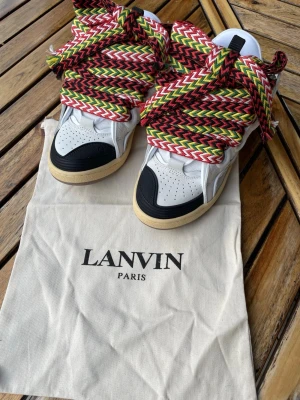 Lanvin sneakers curb - Lanvin sneakers i vitt och svart läder med beige sula och riktigt breda, färgglada skosnören i rött, grönt, svart och vitt zigzagmönster. Klassisk siluett med perforerad tå och kontrastdetaljer. Kommer med dustbag från Lanvin.
