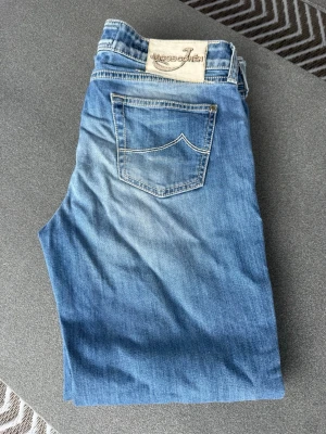 Blå jeans från Jacob Cohen - Snygga blå jeans från Jacob Cohen med klassisk femficksmodell och ljus tvätt. Jeansen har en avslappnad passform och detaljerade sömmar på bakfickan. Tillverkade i mjukt denimtyg som ger en skön känsla och stilren look.
