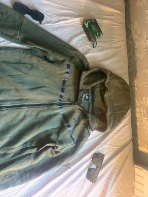 Grön hoodie med huva från Nike - Snygg grön vindjacka från Nike med huva och hel dragkedja framtill. Jackan har svarta detaljer och Nike-logga på bröstet. Perfekt för blåsiga dagar och har en sportig look med bekväm passform.Kan gå ner något i pris vid en riktigt snabb och smidig affär! 