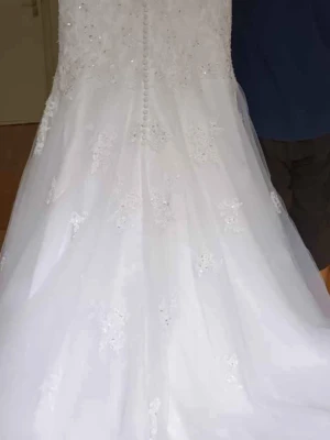 Vit långklänning med spets och paljetter på bra pris  - Elegant vit långklänning med transparent axelparti, dekorerad med spetsdetaljer och paljetter. Klänningen har knappar längs ryggen och ett utsvängt fall. Perfekt för dig som vill ha en romantisk look med extra glitter. Med etiketter på. Original pris 4900 