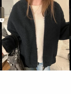 Svart teddyjacka med dragkedja - Mysig svart teddyjacka med dragkedja framtill och avsl sopade sopade ärmar. Jackan sopade har en oversized passform och är gjord i fluffigt teddy-material som ger en trendig look. Perfekt att slänga på sig över en hoodie eller stickad tröja.