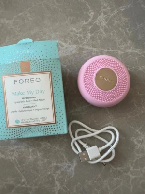 FOREO UFO ansiktsbehandlingsapparat - Säljer en rosa FOREO UFO ansiktsbehandlingsapparat med tillhörande USB-laddare och en förpackning Make My Day- exkluderande masker. Apparatens yta är silikon med guldtonad metall i mitten. Perfekt för dig som vill boosta din hudvårdsrutin med smart teknik.