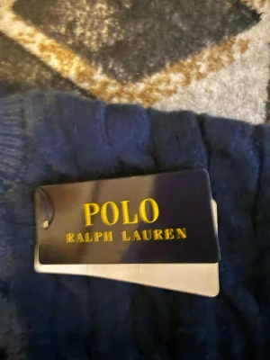 Mörkblå stickad tröja Polo Ralph Lauren - Snygg mörkblå stickad tröja från Polo Ralph Lauren. Klassisk kabelstickad design med ribbade muddar vid hals, ärmslut och nederkant. Perfekt för dig som vill ha en tidlös och stilren look.