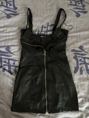 Svart klänning med dragkedja - Svart kort klänning i skinnimitation med dragkedja.