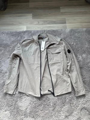 Beige overshirt från C.P. Company - En beige Overshirt från cp company i storlek L men passar M. Helt oanvänd o riktigt snygg för våren nu. Priset kan diskuteras!