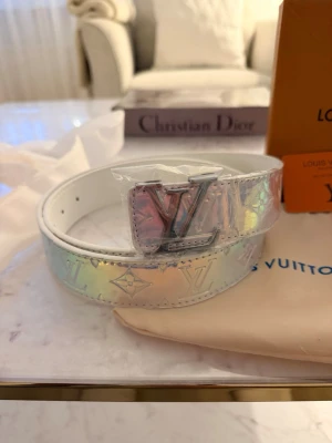 Zaea holografiskt bälte - Snyggt holografiskt bälte från Zara med klassiskt Zara -spänne i silver. Bältet har en skimrande yta i vitt med regnbågseffekt och präglade Zara -loggor. Perfekt accessoar för att lyfta din outfit med en exklusiv touch.