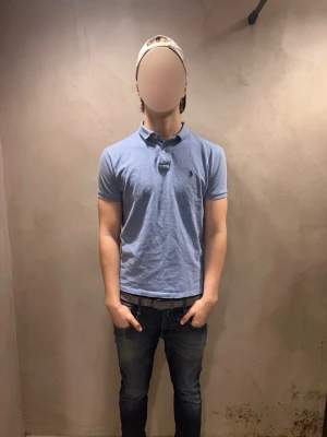 Ljusblå pikétröja från Ralph Lauren - Klassisk ljusblå pikétröja från Ralph Lauren med korta ärmar och krage. Trö har knappar vid halsen och den ikoniska log sop broderad på bröstet. Perfekt till jeans eller shorts för en avslappnad men snygg stil.