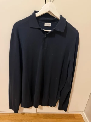 Mörkblå pikétröja John Henric - Aldrig använd!! Ny!!! Nypris 999:- Klassisk mörkblå långärmad pikétröja från John Henric i mjukt material. Tröjan har krage, knäppning med två knappar och ribbade muddar vid ärmsluten. Perfekt för en stilren och avslappnad look. 
