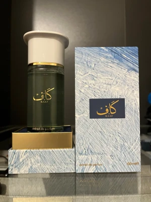 KAAF Extrait de Parfum 100ml - Lyxig parfym från KAAF i en elegant grön glasflaska med vit och gulddetaljerad kork. Flaskan rymmer 100 ml och kommer i en stilren blåvit förpackning med guldfärgad text. Perfekt för dig som vill ha en unik och exklusiv doft.
