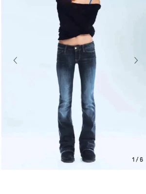 Mörkblå bootcut jeans med slitningar - Snygga mörkblå bootcut jeans med slitningar och lätt tvättade detaljer på låren. Jeansen har låg midja och klassisk femficksdesign. Perfekta för en avslappnad och trendig look.