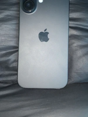 Svart iPhone 16 - Säljer en svart iPhone 16 med stilren design och rundade kanter. Baksidan är matt och har en enkel kamera med blixt. Apple-loggan syns tydligt på baksidan. Skärmen är stor och täcker nästan hela framsidan. Perfekt för dig som gillar snygg och modern mobil. Box medkommer samt kvitto finns o hämta på Gotland annars postar jag den tack på förhand👍