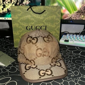 Brun keps från Gucci - Säljer en brun keps från Gucci med klassiskt GG-monogram i beige och mörkbrunt. Kepsen har böjd skärm och justerbar rem baktill. Materialet är canvas med detaljer i läder. Perfekt för dig som gillar exklusiva accessoarer.