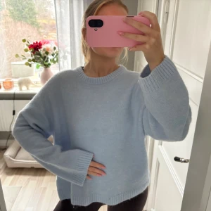 Ljusblå oversized stickad tröja - Mysig ljusblå stickad tröja med rund hals och ribbade muddar. Tröjan är oversized och har långa ärmar, perfekt för att få en avslappnad look. Materialet ser ut att vara mjukt och fluffigt, vilket gör den extra bekväm.