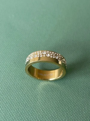 Guldfärgad ring med vita stenar  - Snygg guldfärgad ring från Edblad med vita stenar i ett mönster på halva ringen. Ringen har en bred och slät design som känns modern och stilren.  Strl 17,5