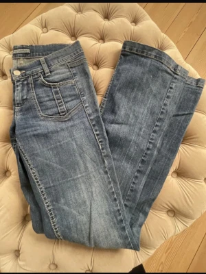 Lowwaist blå bootcut jeans - Säljer ett par klassiska lågmidjade blå bootcut jeans med kontrastsömmar. Jeansen har fem fickor och en liten broderad Lee-logga på myntfickan. 