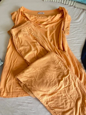 Ribbad orange pyjamas från Bonatti - Mysig pyjamas från Bonatti i en härlig orange färg. Setet består av en kortärmad topp och långa byxor i ribbad, mjuk och stretchig trikå. Perfekt för slappa dagar hemma eller sköna nätter. Materialet känns lätt och luftigt mot huden.