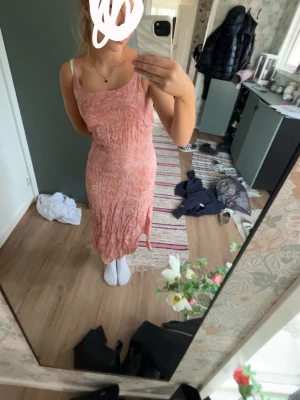 Ljusrosa långklänning med blommönster - Säljer en ljusrosa långklänning med smala axelband och blommigt mönster. Klänningen har en figurnära passform och är tillverkad i ett lätt material som passar perfekt till varmare dagar. Enkel och stilren design..