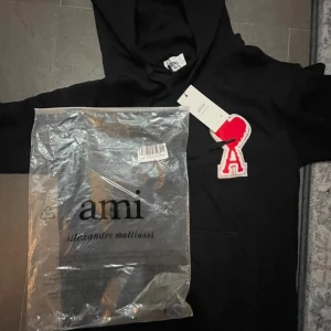  Ami Paris hoodie - Svart hoodie från Ami Paris med ikonisk röd hjärta-A patch på bröstet. Helt ny tröja som jag fick i present och inte passar min klädstil! Säljes billigt för vill få bort den. Storlek M