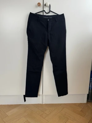 Svarta kostymbyxor Tiger of Sweden  - Snygga svarta kostymbyxor med smal passform och klassisk design. Byxorna har två sidofickor fram och två bakfickor med knapp. Perfekta för en stilren look och passar till skjorta eller t-shirt. Materialet känns mjukt och har en lätt stretch. Storlek 44. Nypris 1399 kr 