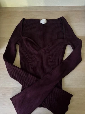 Mörklila ribbad långärmad topp - Snygg mörklila ribbad topp med v-ringning och lång ärm. Figurnära passform som framhäver siluetten och ger en trendig look. Perfekt att styla med jeans eller kjol för en cool vibe.