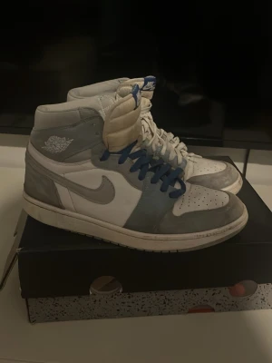 Air Jordan 1 Retro High OG Hyper Royal - Snygga Air Jordan 1 Retro High OG Hyper Royal med vit och ljusblå mocka och läder. Klassisk Nike Swoosh på sidan, blå och vita skosnören samt ikoniska Air Jordan-loggan på ankeln. Perfekta för dig som gillar streetwear och sneakers med hype.