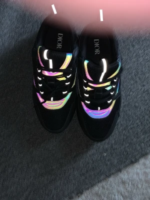 Svarta B22 med mesh och reflex  - Säljer ett par svarta sneakers med cool regnbågseffekt längs sidorna och vita detaljer. Skorna har en chunky sula och meshpaneler för extra komfort och stil. Perfekta för dig som vill sticka ut och ha något exklusivt på fötterna. Skorna är helt nya och är oanvända. Säljer de pågrund av storleken. Pris kan diskuteras!!