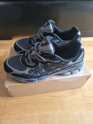 Asics GEL-NYC svart/grå sneakers - Snygga Asics GEL-NYC sneakers i svart och grått med mesh och syntetpaneler. Skorna har en chunky sula och reflekterande detaljer. Perfekta för dig som gillar sportig och modern stil. Klassisk Asics-logga på sidan och bekväm passform.