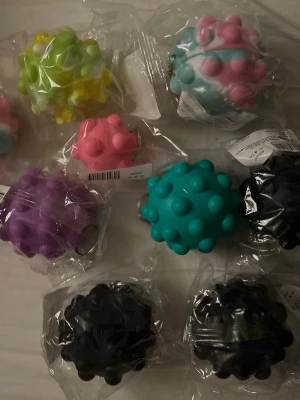Färgglada stressbollar med piggar - Säljer ett gäng massagebollar i olika färger som svart, turkos, rosa, lila, grön och gul. Bollarna är tillverkade i plast. Alla bollar är runda och ligger i plastförpackning. Säljer de för 30kr st alla för 260kr