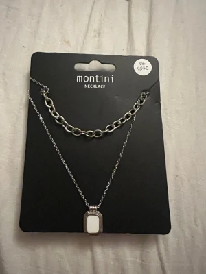 Montini silverfärgat halsbandsset - Tvådelat halsbandsset från Montini i silverfärg. Ena halsbandet har en grov kedja och det andra ett tunnare kedjeband med en rektangulär vit berlock. Snyggt att bära tillsammans för en trendig lager-på-lager-look. 