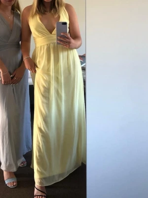 Ljusgul långklänning med korsade band - Snygg ljusgul långklänning med djup v-ringning och korsade axelband i ryggen. Använd en gång.
