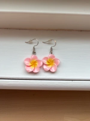 Rosa blommiga örhängen  - Säljer ett par söta örhängen formade som blommor i rosa och gult. De har krokar i metall och själva blomman är gjord av plast. Perfekta för dig som gillar färgglada accessoarer och vill ha en unik touch till din stil.
