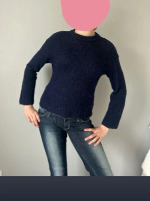 Mörkblå stickad tröja med raka ärmar - Mysig mörkblå stickad tröja med enkel design och raka, lite vidare ärmar. Tröjan har en klassisk rund halsringning och är lätt att matcha till olika outfits. Perfekt för kyligare dagar och ger en avslappnad men snygg look.