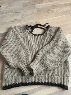 Beige chunky stickad tröja - Chunky stickad tröja i beige med mörkbruna detaljer vid halsringning och nederkant. Tröjan har breda ärmar och ribbstickade muddar. Perfekt för de kommande kalla sommarkvällarna!🩷