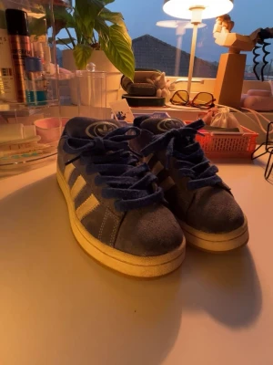 Blå Adidas Campus - Snygga blå sneakers från Adidas med klassiska vita ränder på sidorna och blå mockadetaljer. Skorna har tecken på användning då jag haft de ett tag. Annars är de ett par sköna och coola skor😁🩷