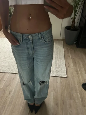 Ljusblå baggy jeans med hål - Säljer ett par ljusblå baggy jeans med raka ben och slitna hål på båda knäna. Jeansen har klassisk femficksmodell, låg midja och är tillverkade i denim. Perfekta för en avslappnad och trendig look.