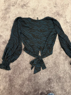 Zebramönstrad omlottopp med knyt - Snygg zebramönstrad omlottopp i mörkblått och svart med långa puffärmar och knyt i midjan. Toppen har v-ringning och resår vid ärmsluten för en trendig look. Perfekt för dig som vill sticka ut lite extra.
