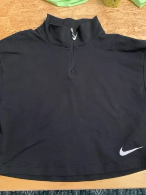 Svart croppad tröja från Nike - Svart croppad polotopp från Nike med korta ärmar och half zip-dragkedja framtill. Helt nyskick! 